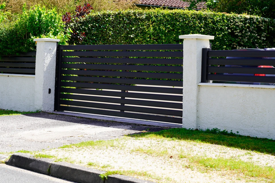 Entrée résidentielle avec portail coulissant automatique en aluminium anthracite à lames horizontales, intégré dans clôture maçonnée blanc cassé avec piliers béton