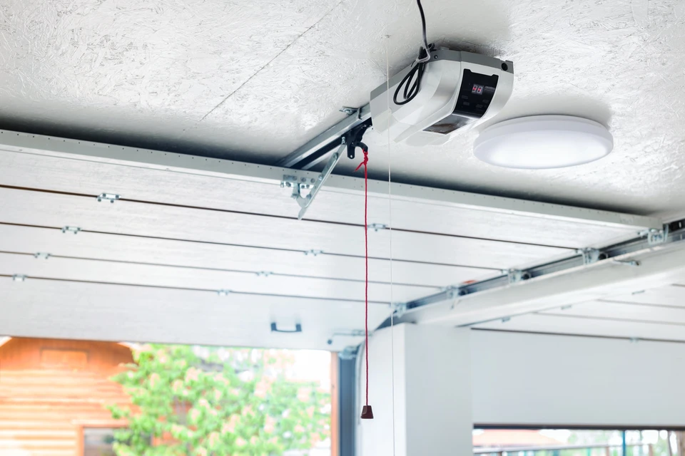 Garage résidentiel avec porte sectionnelle blanche partiellement ouverte laissant voir la végétation extérieure