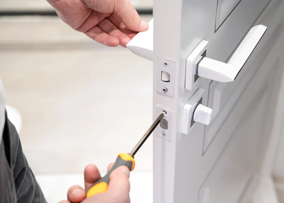 Serrurier utilisant un tournevis pour installer ou réparer une serrure de porte, en se concentrant sur le travail précis de fixation du mécanisme de serrure