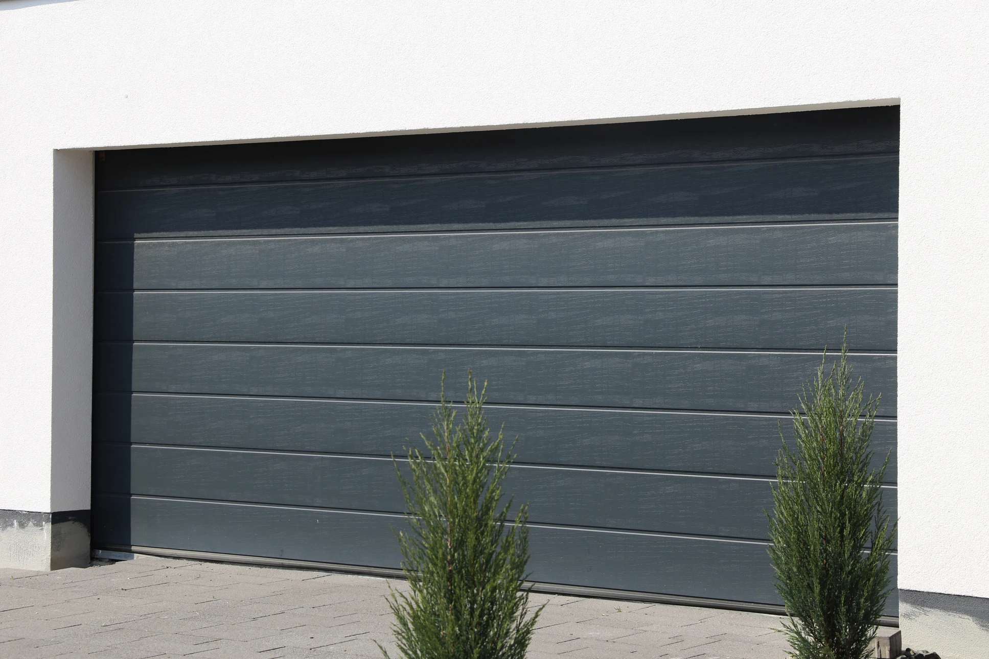 Extérieur résidentiel moderne avec porte de garage sectionnelle grise à quatre panneaux horizontaux lisses, intégrée dans façade blanche contemporaine