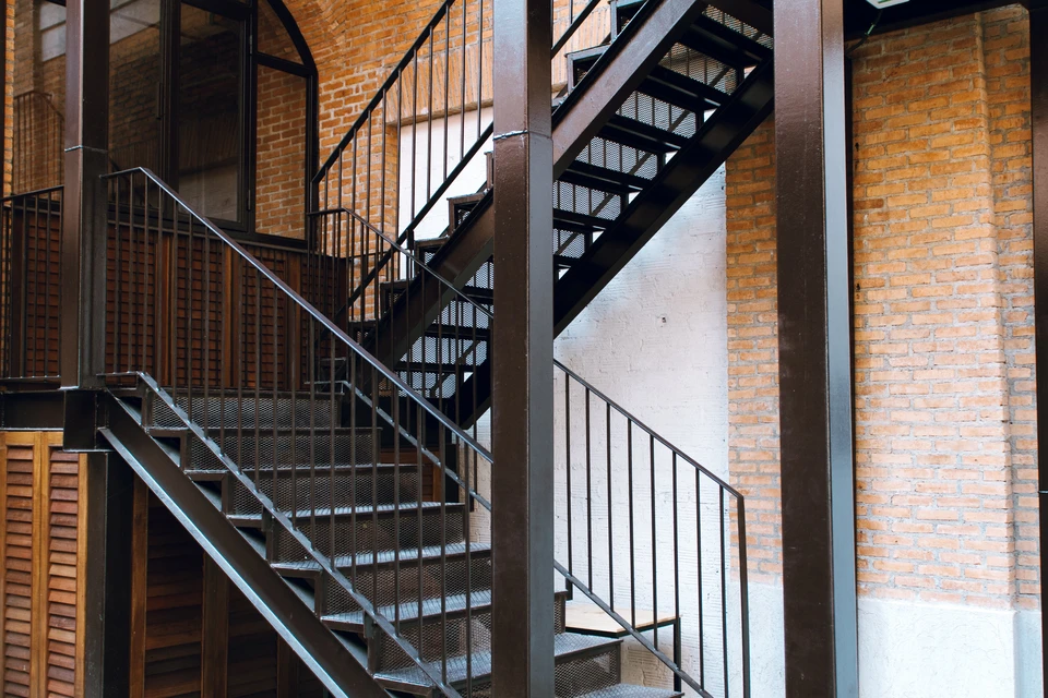 Escalier métallique industriel avec palier intermédiaire et garde-corps à barreaux verticaux dans un environnement de briques apparentes