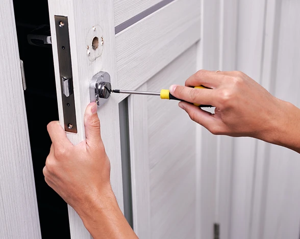 Serrurier utilisant un tournevis pour installer ou réparer une serrure de porte, en se concentrant sur le travail précis de fixation du mécanisme de serrure